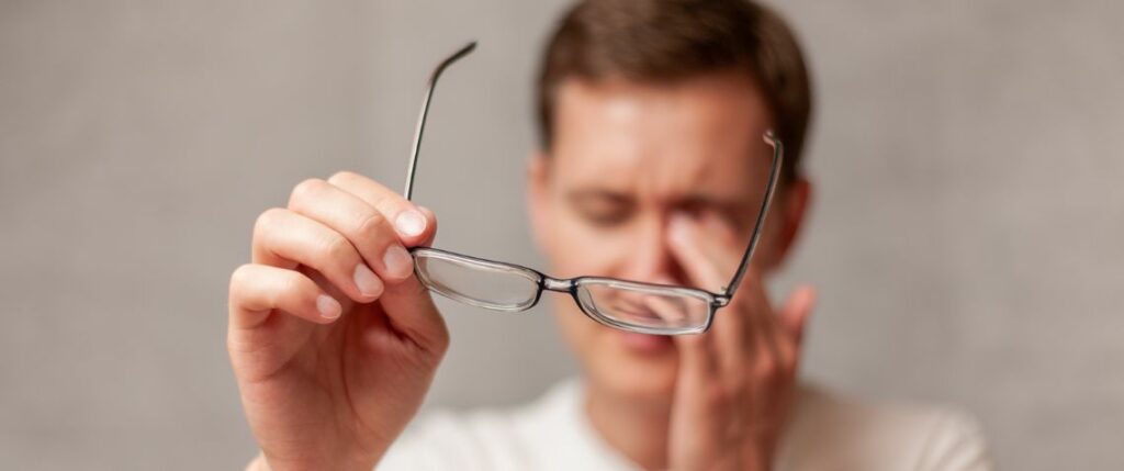 Man holding glasses rubbing his eyes