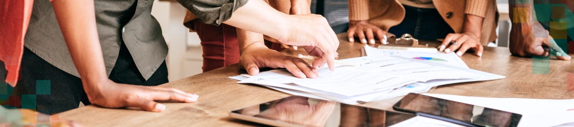 People's hands on a table analyzing papers and electronic devices.