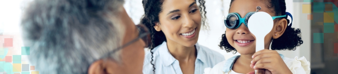 Young girl in an eye exam with her mom next to her smiling.