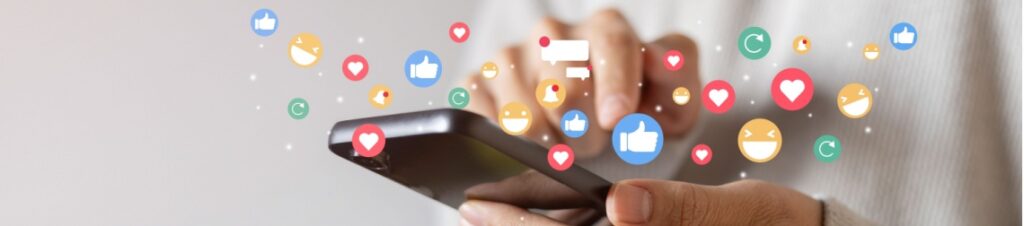A hand holding a smart phone with icons of hearts, thumbs ups, and smiles coming up from the screen